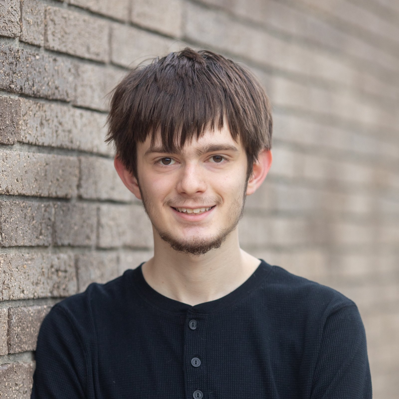 Jared Baesen leaning against a sone brick-textured wall